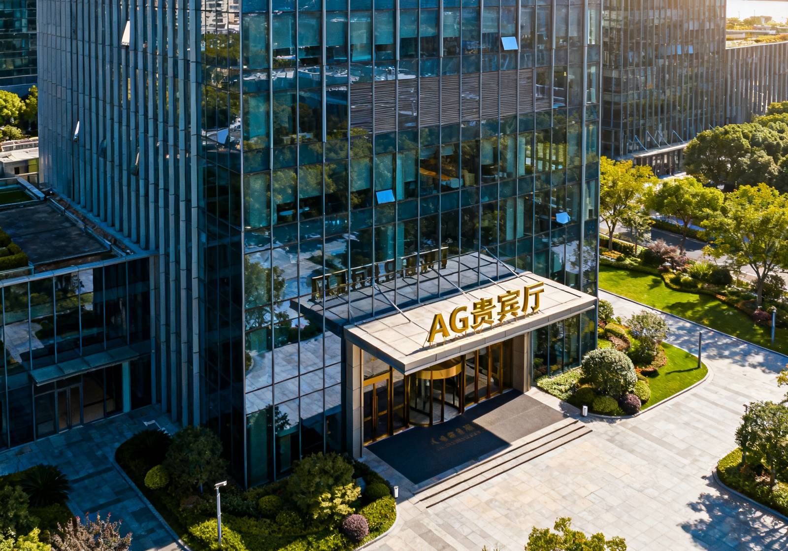 AG贵宾厅上海总部所在的恒隆商务中心A座大楼外观航拍，现代玻璃幕墙建筑在阳光下熠熠生辉，大楼入口处可见AG贵宾厅的镀金标识牌，周边绿化优美。